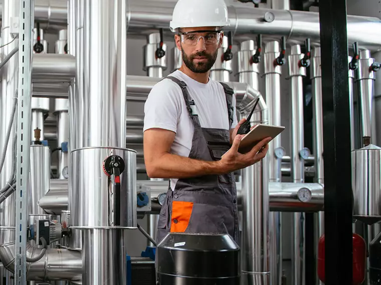 Private Networks application - Man in a hard hat and overalls standing in front of a machine with a tablet in one hand